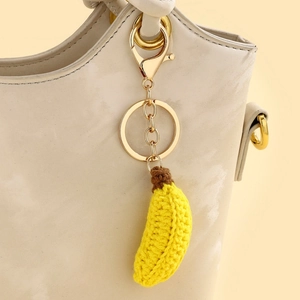 Handgemaakte gehaakte banaan sleutelhanger hangend aan een beige lederen tas