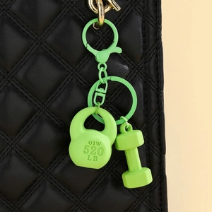 Detail showing neon green kettlebell and dumbbell keychain hanging on a black leather bag