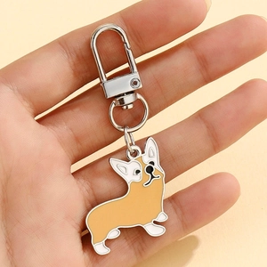 Main tenant un porte-clés Corgi en alliage marron et blanc avec mousqueton argenté