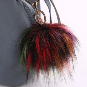 Close-up of a fluffy multi-color faux fur pompom keychain on a grey handbag