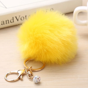 Gros plan sur un porte-clés pompon jaune vif en fausse fourrure avec anneau doré et strass