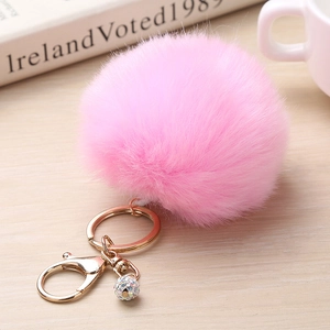 Détail d'un porte-clés en fourrure rose avec boule en strass sur une surface en bois