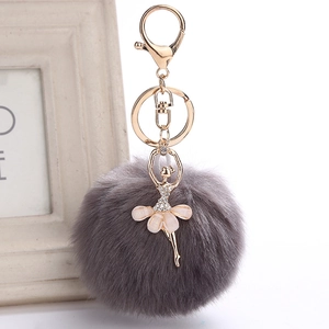 Close-up of a grey faux fur pom pom keychain with a gold rhinestone ballet girl pendant