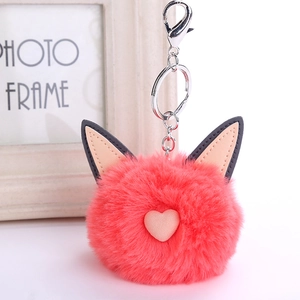 Pink faux rabbit fur cat ear keychain with heart decor on a warm wooden frame background