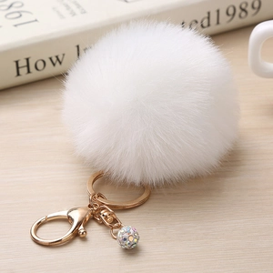 Détail du porte-clés pompon blanc avec anneau doré et perles strass sur table en bois clair