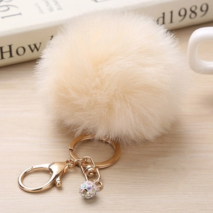 Détail d'un pompon en fausse fourrure beige avec fermoir doré et perle strass arc-en-ciel