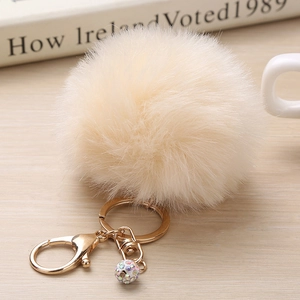 Détail d'un porte-clés pompon en fausse fourrure crème avec mousqueton doré et boule strass