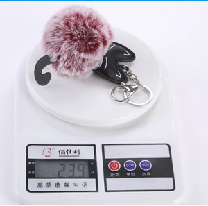 Detail shot of a cute cat plush pompom keychain weighing 23.9g on a digital scale