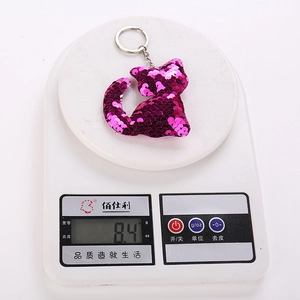 Reflective rose red sequin kitten keychain accessory with metal ring on a white scale