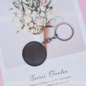 Detail of a round dark wood keychain with silver ring on an illustrated floral background card