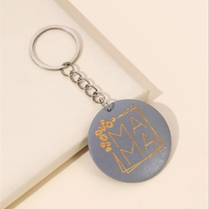 Détail d'un porte-clés gris avec gravure MAMA dorée et motifs floraux sur fond blanc