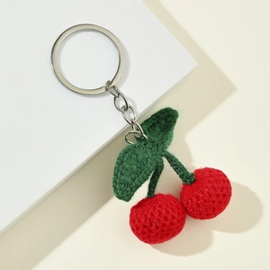 Handmade crochet cherry keychain with red knitted berries and green leaves on a white stand