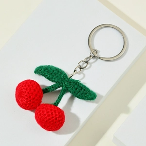 Handmade crochet cherry keychain with red knitted berries and green leaves on a white stand