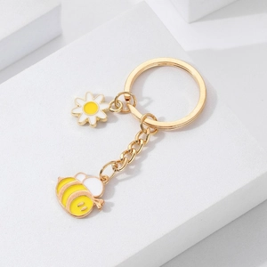 Détails rapprochés de porte-clés marguerite et abeille dorés sur un support blanc pur