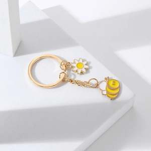 Détail d'un porte-clés doré avec pendentif marguerite blanche et petite abeille rayée jaune