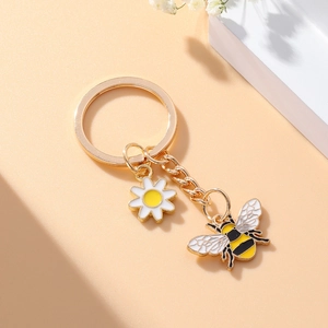 Détails du porte-clés doré avec pendentifs abeille et marguerite blanche sur décor