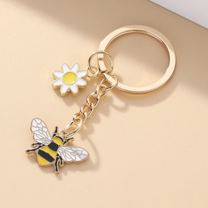 Porte-clés doré avec charms abeille en émail et marguerite sur fond beige neutre