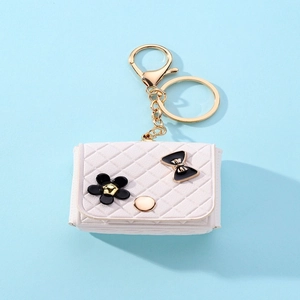 Macro shot of white quilted mini bag keychain with black flower and golden metal clasp