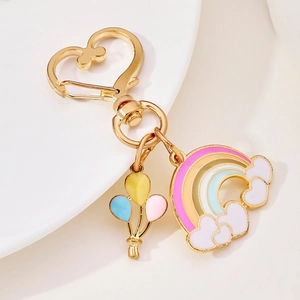 Golden heart-shaped keychain with colorful enamel rainbow and balloon charms on a white tray