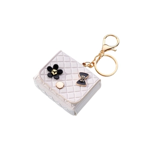 Mini quilted cream bag keychain with black flower charm and gold hardware on white background