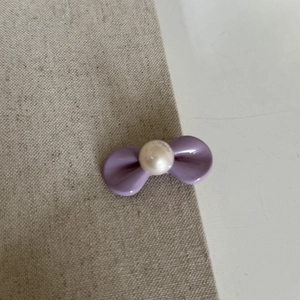 Detailansicht einer lila Schleifen-Haarspange mit Perle auf beige strukturiertem Stoff