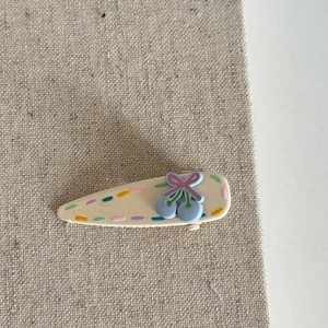 Cute cream cherry hair clip with blue glaze and pink bow on textured fabric