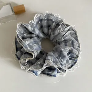 Close-up of blue plaid scrunchie with white lace trim and embroidered bow patterns