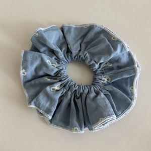 Détail d'un chouchou bleu-gris avec motifs de nœuds beige et bordure blanche