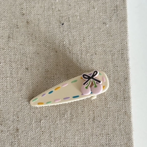 Cute cream cherry hair clip with colorful dash patterns on textured beige linen background