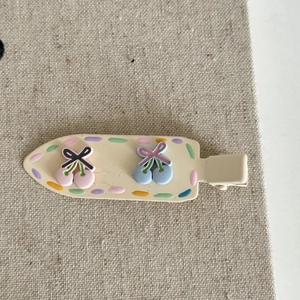 Close-up of cute cream hair clip with 3D cherry accents and colorful polka dots on fabric