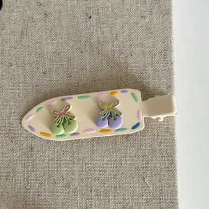 Detail of cream-colored duckbill hair clip with colorful dots and resin cherry charms