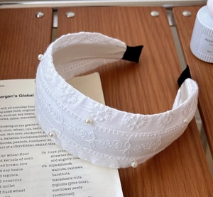 Détail d'un bandeau en dentelle blanche avec broderie florale et perles délicates
