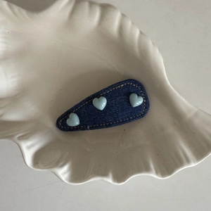 Detail of blue denim BB hair clip featuring three light blue heart beads on a white tray