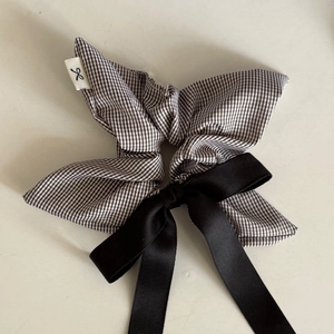 Close-up of black and white gingham scrunchie with long satin bow and woven brand label