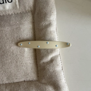 Gros plan d'une pince à cheveux crème à pois bleus sur une surface en tissu texturé