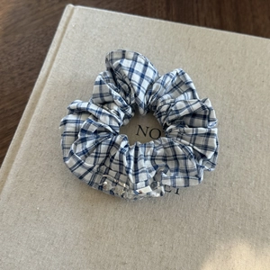 Close-up of blue and white checkered scrunchie with silver metal charm on a book