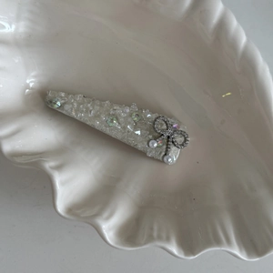 Elegant silver bow hair clip with crystals and white pearls on ceramic shell tray