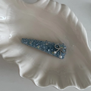 Detail of light blue beaded crystal hair clip with silver bow and pearls on shell tray