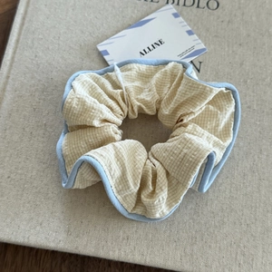 Close-up of beige plaid scrunchie with blue trim on a minimalist aesthetic background