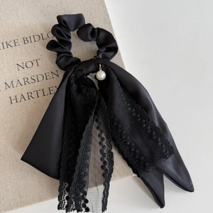 Détail d'un chouchou en satin noir avec rubans en dentelle et perle blanche