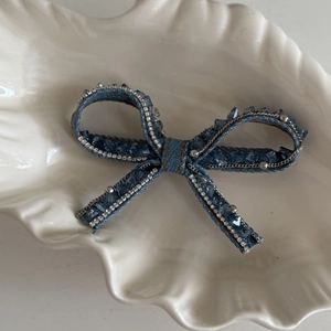 Luxury blue denim bow hair clip with crystals and silver rhinestones on a white shell plate