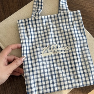 Close-up of blue and white checkered canvas tote bag with Alline text on wooden table