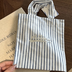 Detail shot of a blue and white striped canvas tote bag with shiny silver Allure text
