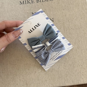 Close-up of three blue striped fabric bow hair clips on a branded display card