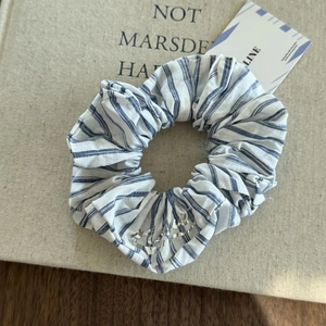 Blue and white striped scrunchie with silver letter charm on textured background