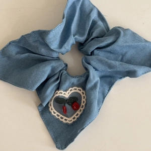 Close-up of blue denim scrunchie with bow tie and cherry heart embroidery detail