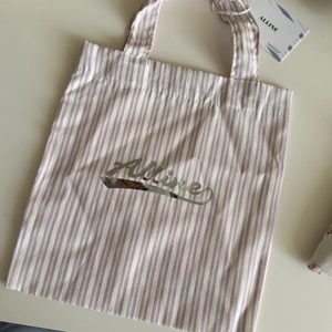 Detailed macro view of purple and white striped canvas tote bag with Alline metallic logo