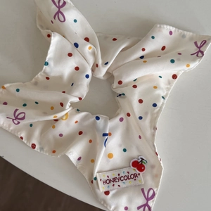 Detail of cream silk scrunchie with colorful dots and cherry brand tag on white desk