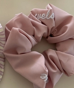 Detailed shot of pink satin scrunchie featuring white uelo letter embroidery