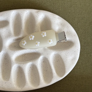 Dettaglio del fermaglio per capelli con fiori 3D bianchi su base in acrilico crema